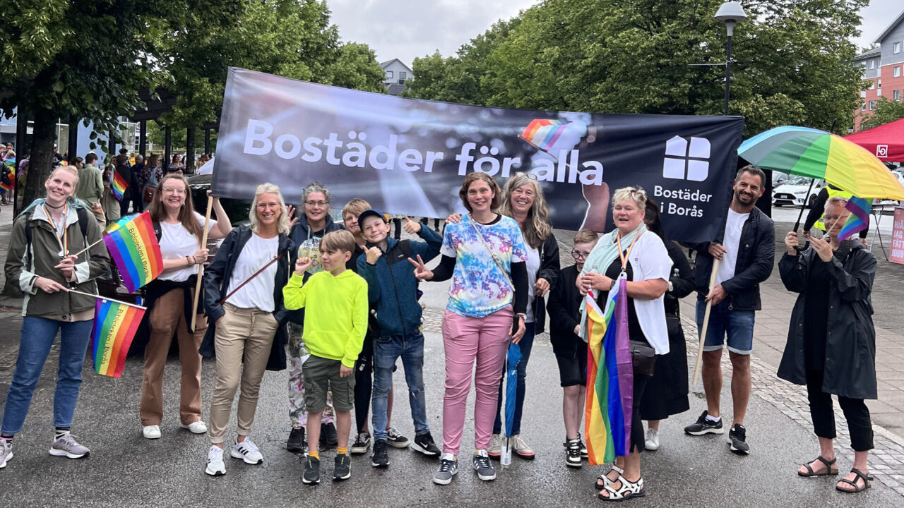 Personal på Bostäder i Borås deltar i Pride-tåget 2023 med en stor banderoll med texten "Bostäder för alla" och Pride-flaggor.
