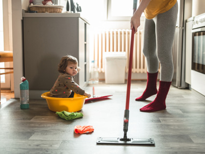 Ung mamma  utför hushållsarbete medan ett litet barn  tittar på.