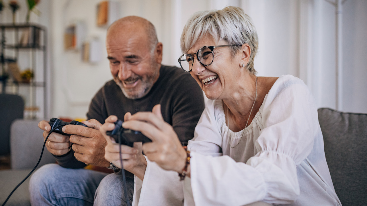 Medelålders par sitter i soffan och skrattar och spelar tv-spel
